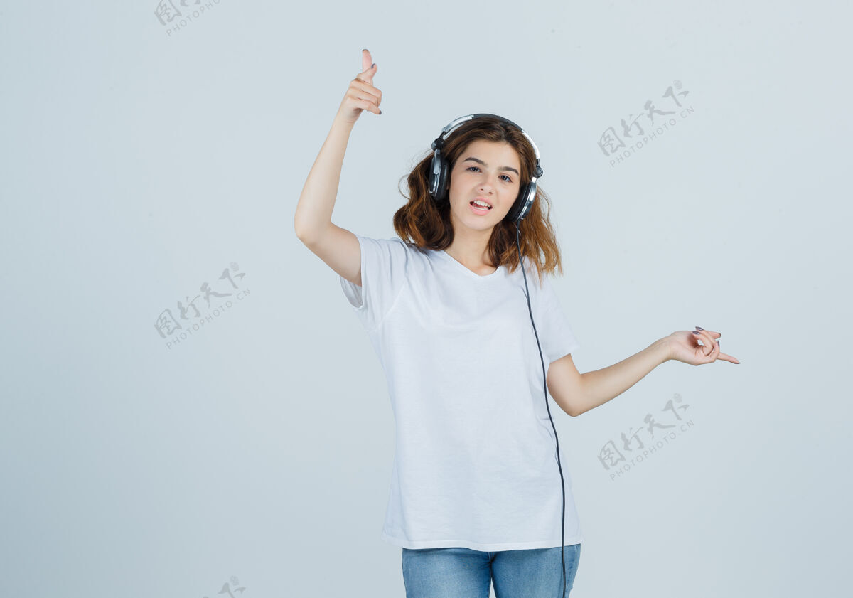 音乐年轻女性一边用耳机欣赏音乐一边指指点点 身穿白色t恤 牛仔裤 看上去很开心 正对着前方看惊喜愉悦人
