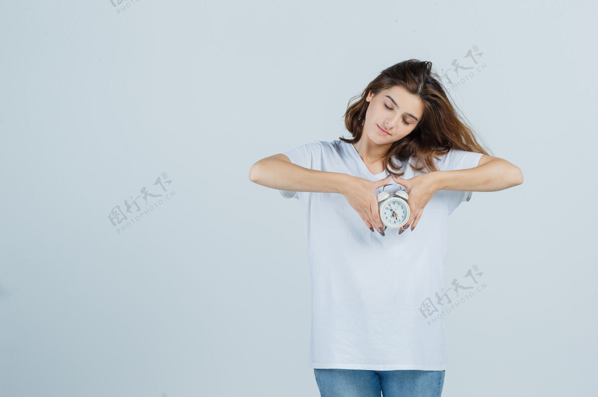 美容照片中的年轻女性手持闹钟 身穿白色t恤 牛仔裤 端庄优雅的前视图惊喜模型时钟
