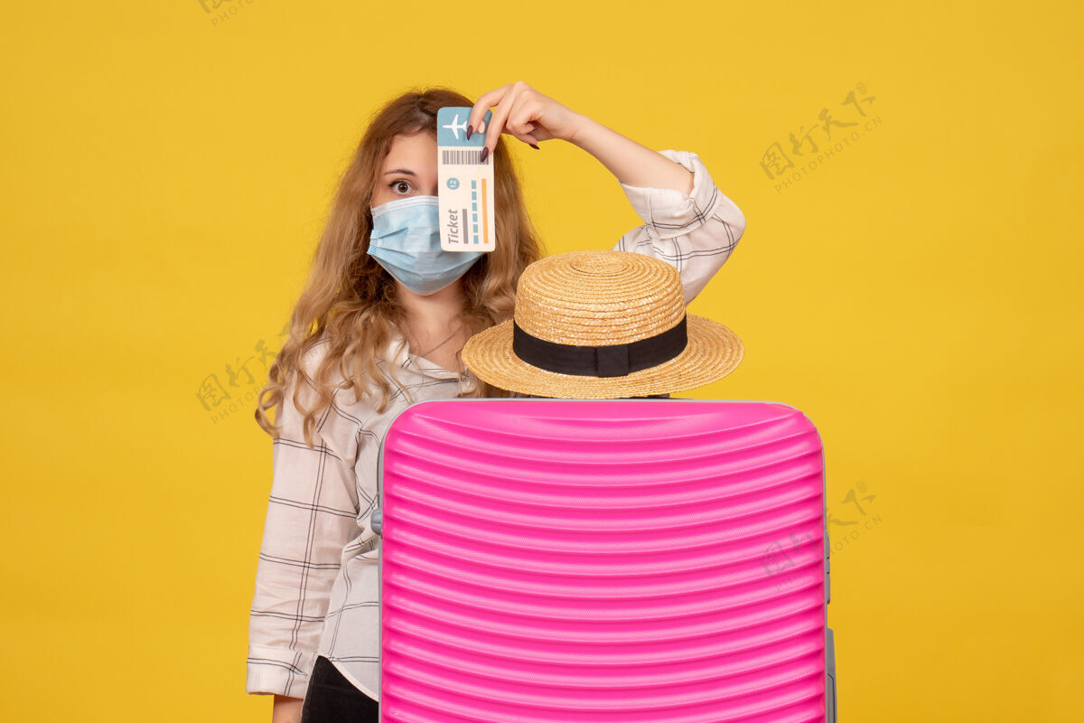 站着戴着面具的年轻女士的俯视图 展示着车票 站在她的粉色包后面上衣包漂亮