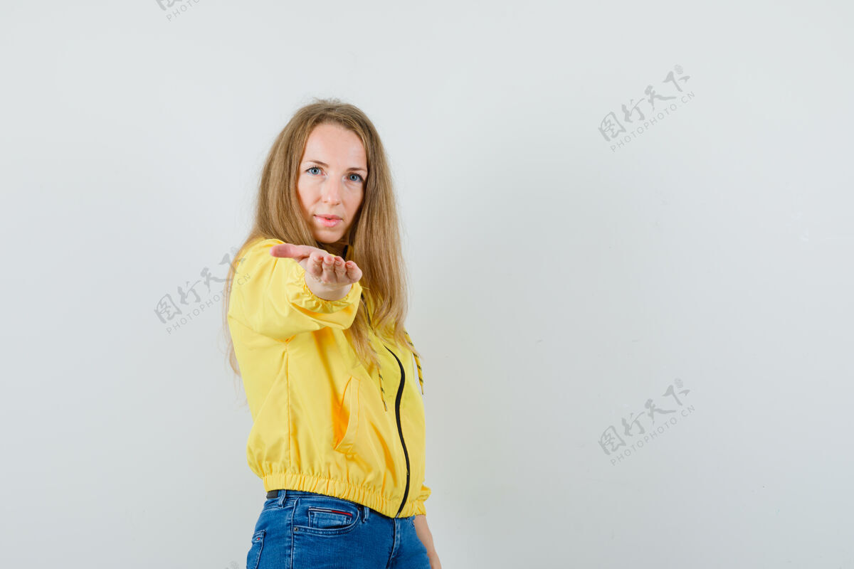 成人年轻女子穿着黄色的棒球服和蓝色的牛仔裤 看起来很严肃正面图牛仔裤女性时尚
