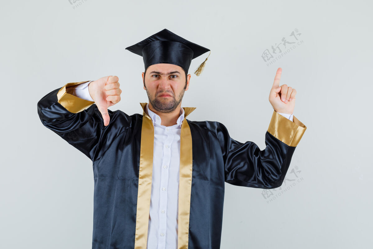 毕业年轻人指着头 穿着毕业制服 拇指朝下 神情阴郁正视图站立男人衬衫