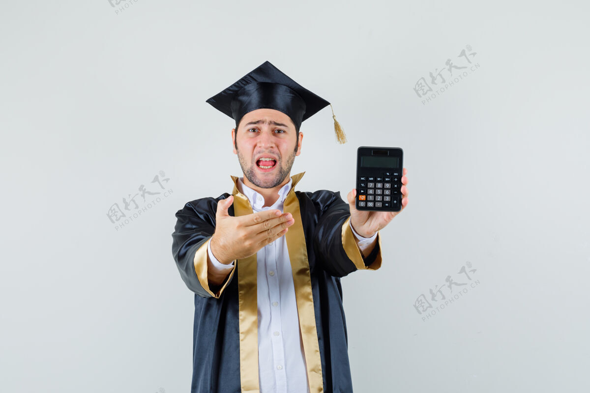 计算器一个穿着毕业制服的年轻人正在展示计算器 他看起来很困惑 正对着我看前面男人模特