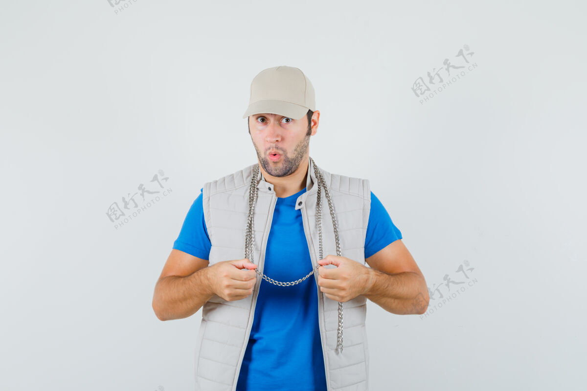 年轻年轻人穿着t恤 夹克 戴着帽子 手里拿着他的项链 看上去很惊讶 前视图成功项链T恤