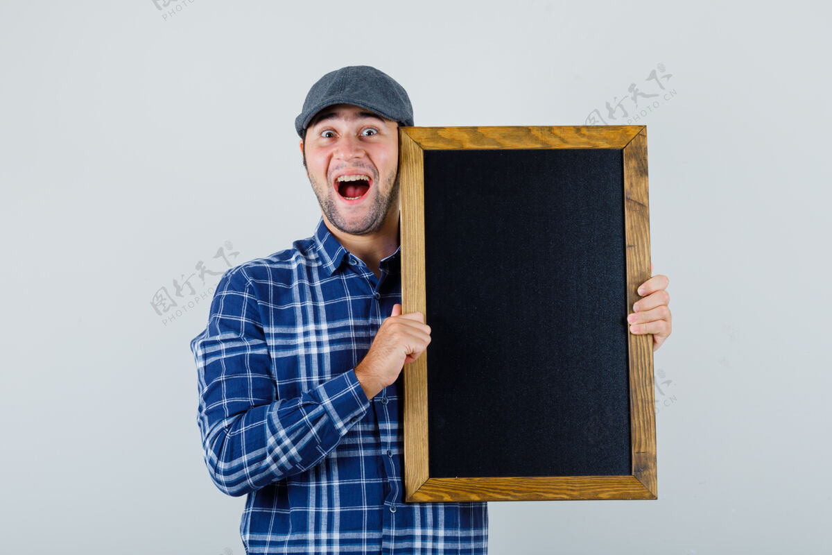 肖像年轻人拿着黑板 穿着衬衫 戴着帽子 看上去很快乐 正对着窗外模特聪明男人