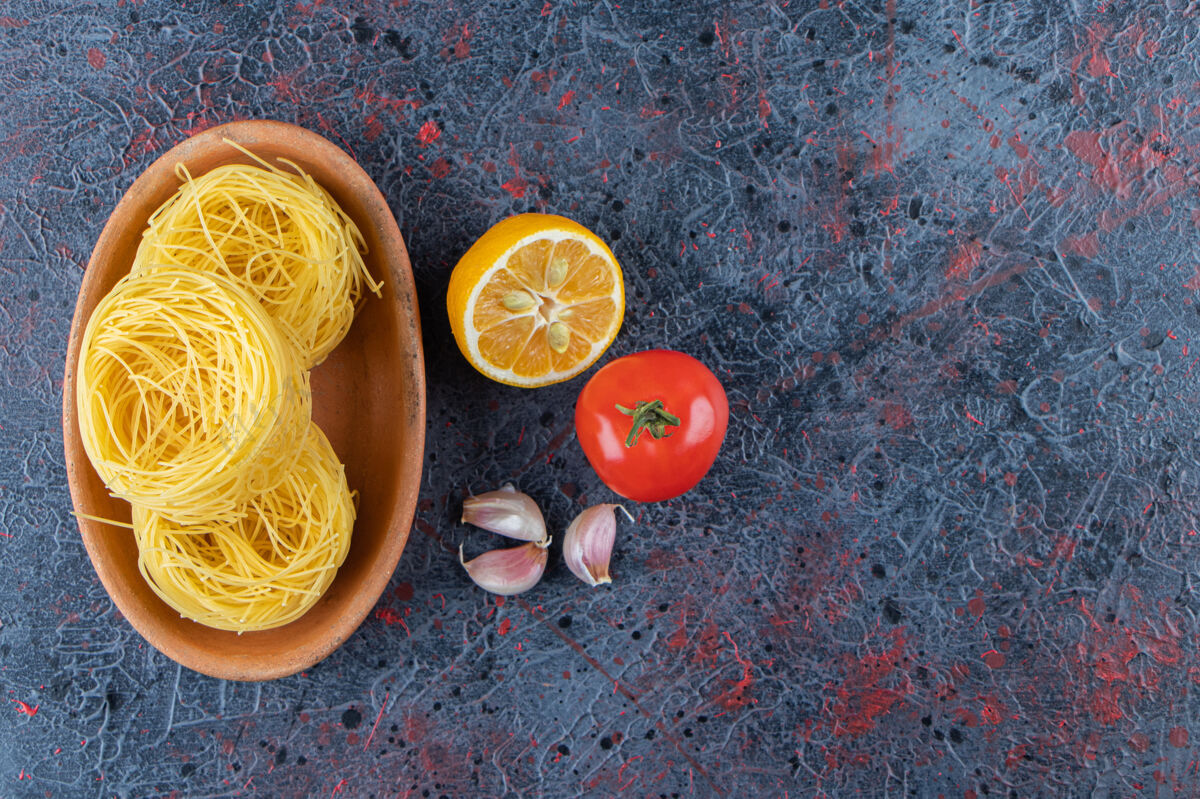 生的一块木板 上面是生的干巢面食 背景是柠檬和新鲜的红色番茄红色未经准备的烹饪