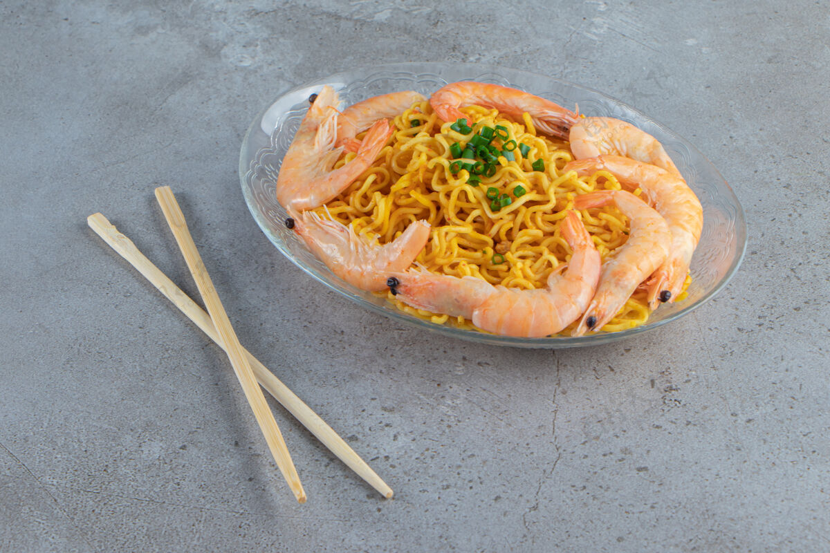亚洲菜虾和面条放在玻璃盘上 旁边是筷子 背景是大理石面食烹饪虾