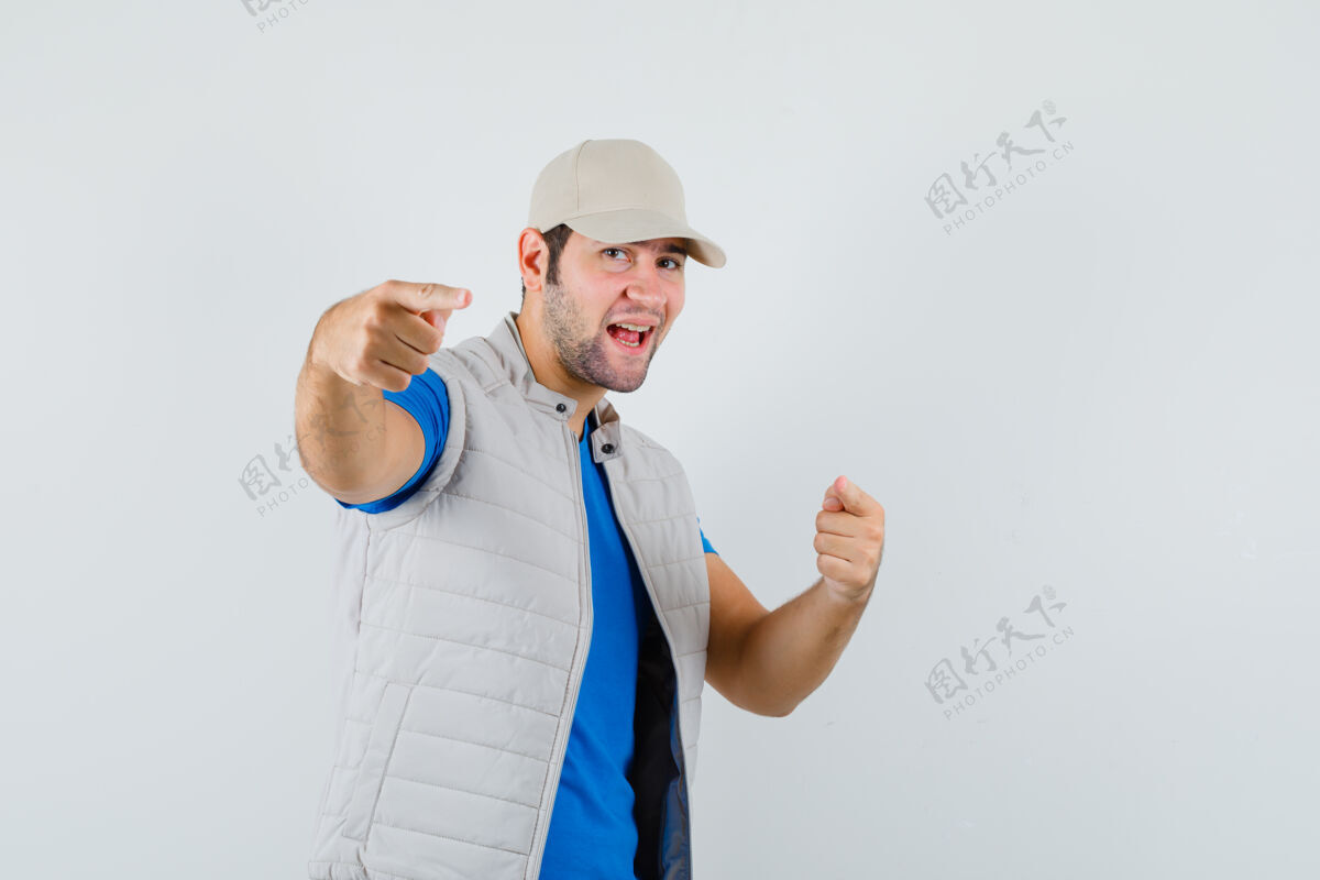 男人一个穿着t恤衫 夹克衫 帽子的年轻人指着摄像机 看上去很活泼成功站立欢呼
