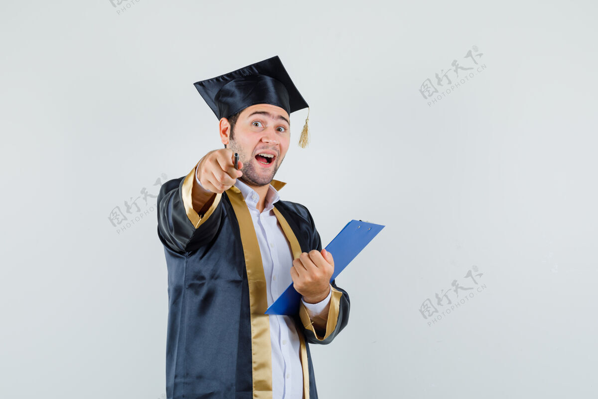 前面年轻人拿着剪贴板 指着相机 穿着研究生制服 看上去很乐观 正对着镜头年轻帅哥毕业