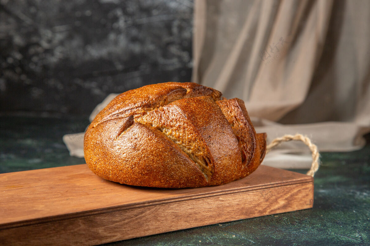 整个整个新鲜的黑面包在黑暗的表面棕色木砧板的侧视图食品面包百吉饼