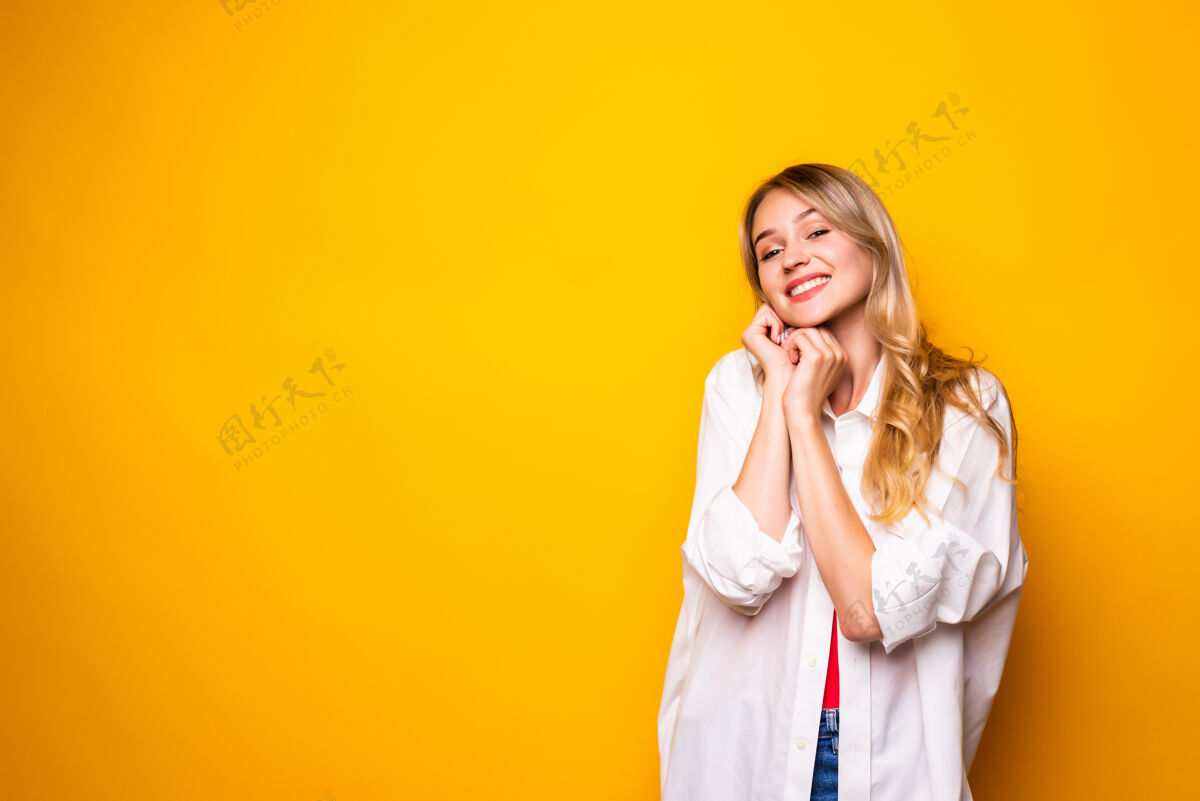 女人美丽的年轻女子手拉着下巴 微笑着 站在黄色的墙上站立夏天金发