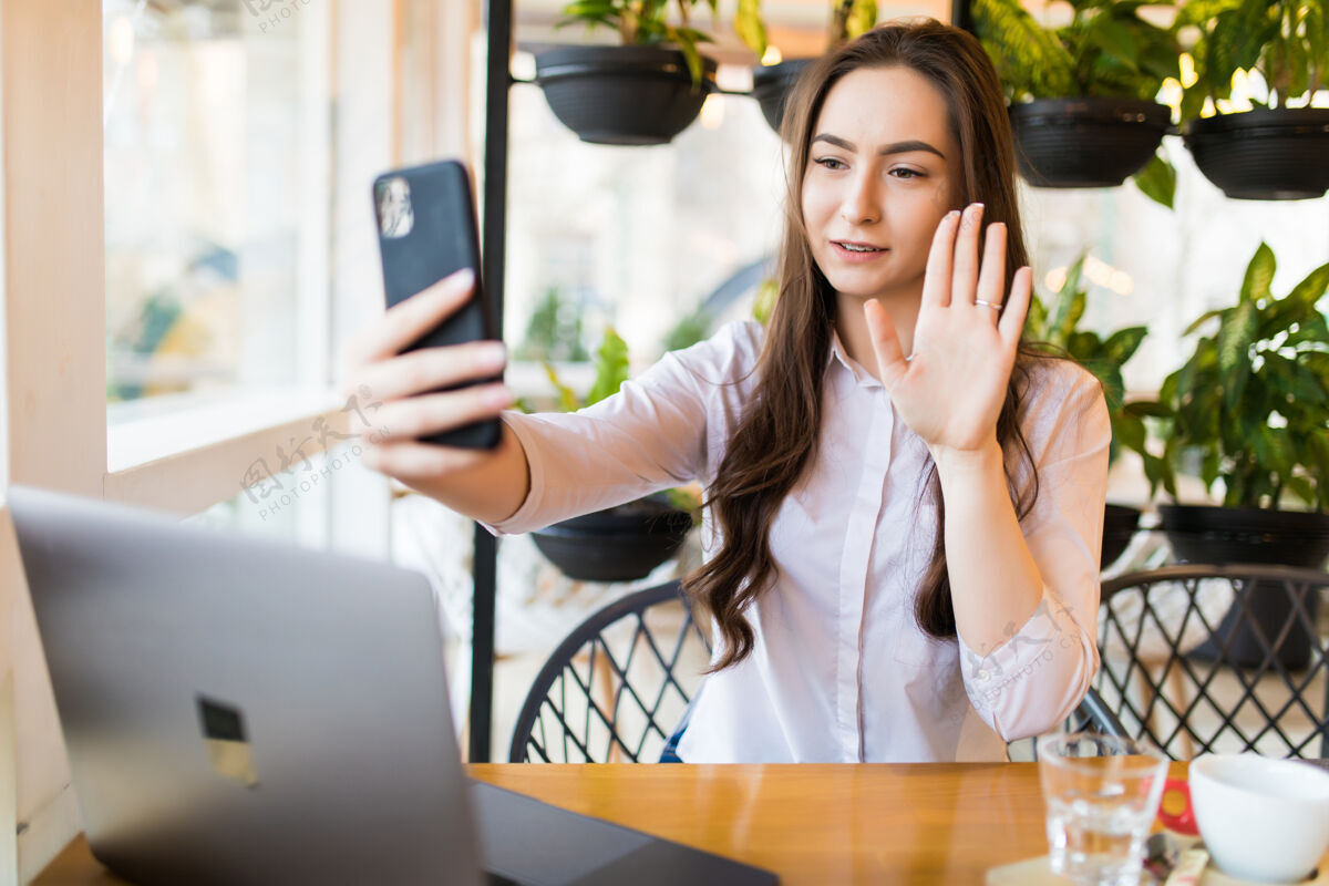 聊天年轻开朗的女人在智能手机上拍照和朋友聊天 迷人的笑脸潮人女孩坐在咖啡馆里用手机自拍手机积极放松