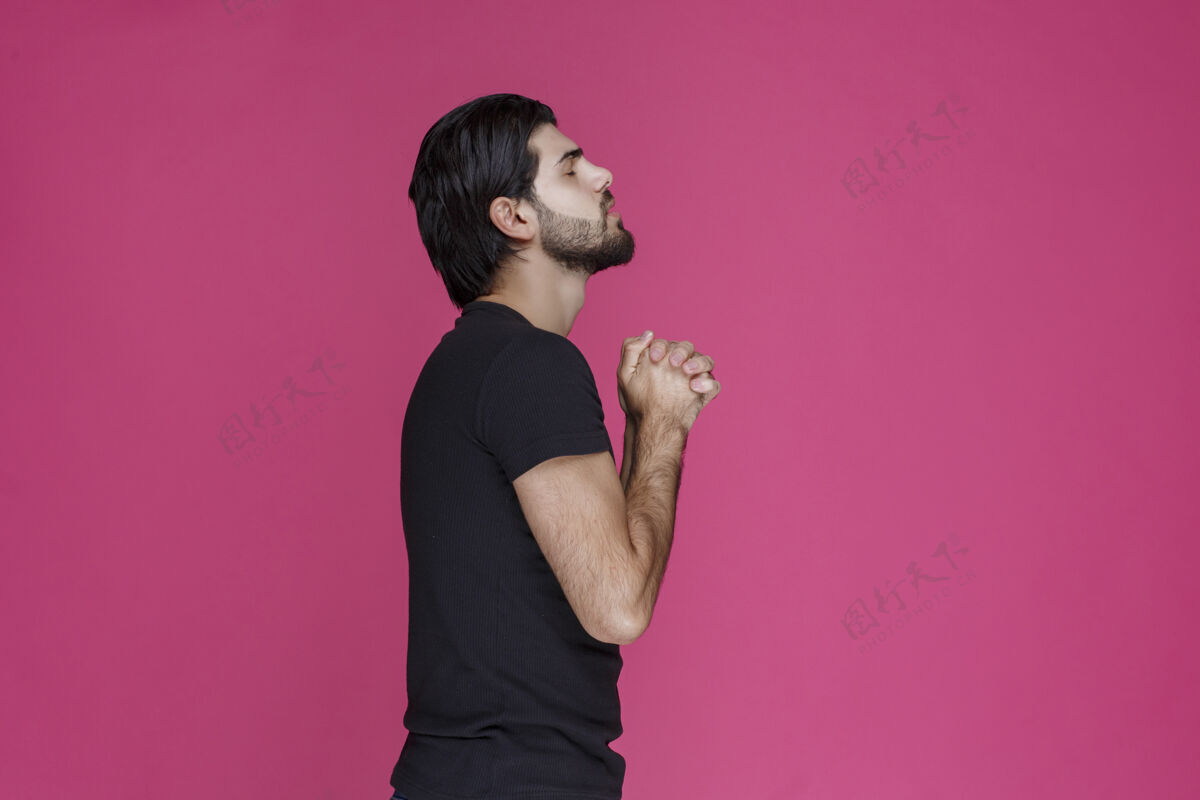 工人穿黑衬衫的男人在祈祷 梦想着什么姿势愿望祈祷