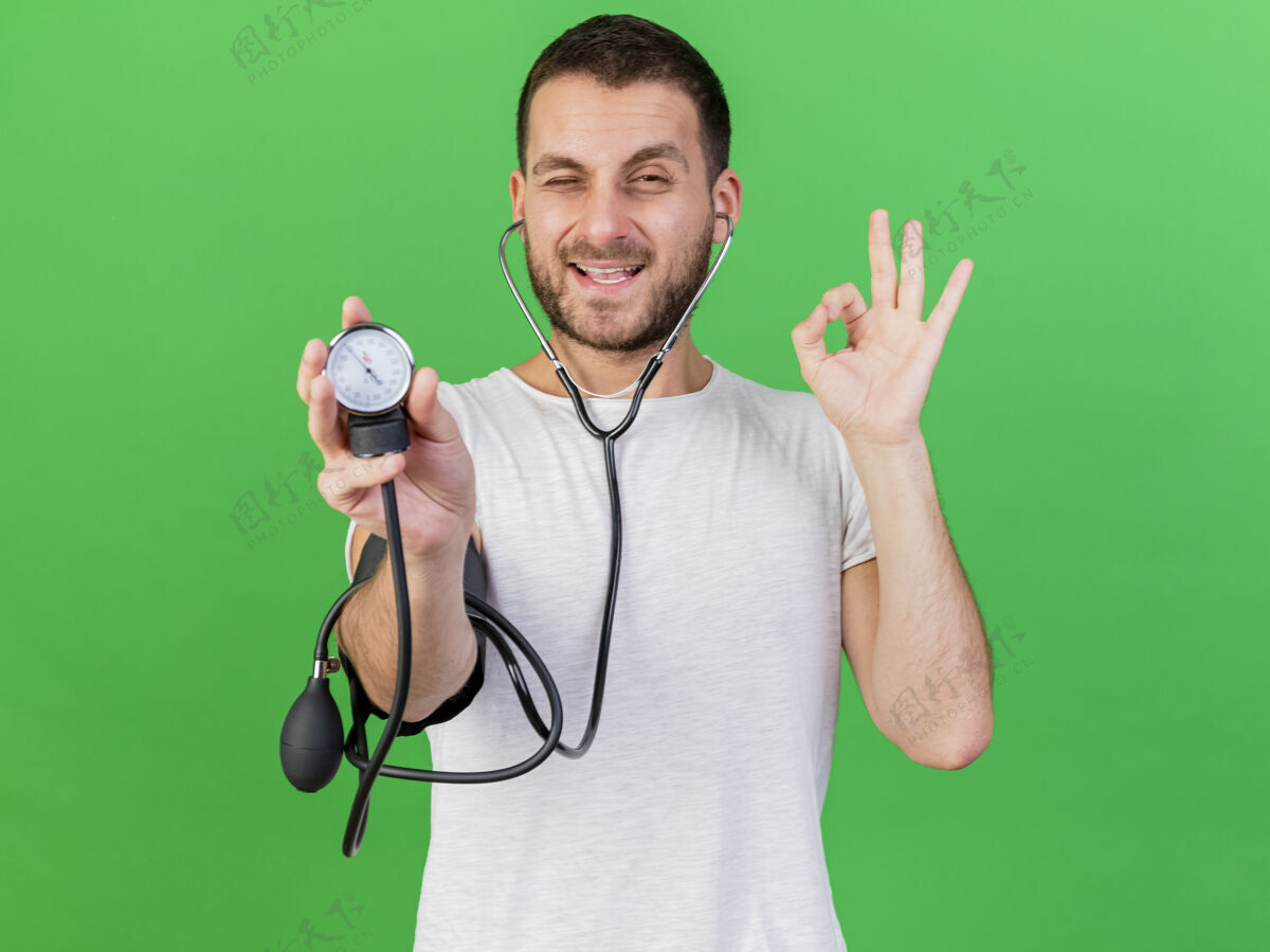 自己的年轻的病人戴着听诊器 用血压计测量自己的血压 在绿色背景上显示出良好的姿势 这让他很高兴听诊器手势好的