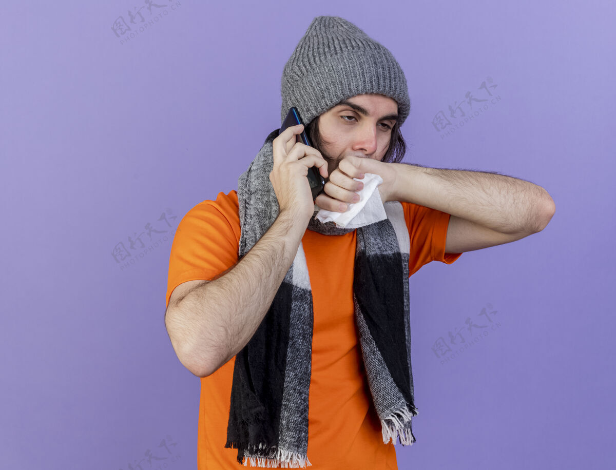 电话看着身边虚弱的年轻病人戴着冬天的帽子 戴着围巾讲电话拿着餐巾 用手擦着鼻子隔离在紫色的背景上餐巾抱着壁板