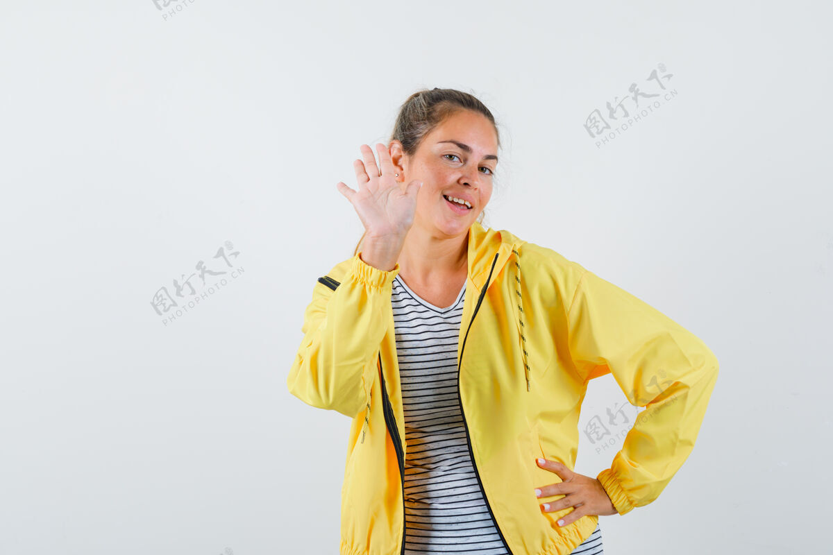 女人一个金发女人一只手放在腰上 另一只手伸开 像是在问候一个穿着黄色棒球服和条纹衬衫的人 看起来很开心夹克肖像可爱