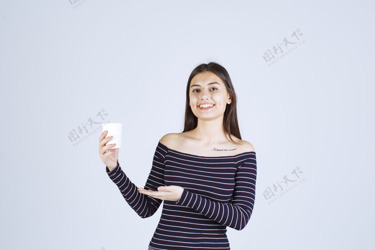 姿势穿着条纹衬衫的女孩拿着一个塑料咖啡杯 看起来很积极服装人体模特女人