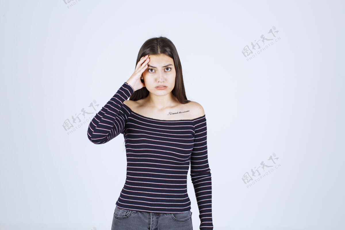 模特穿着条纹衬衫的女孩抱着她的头 因为她筋疲力尽或头痛休闲雇员成人