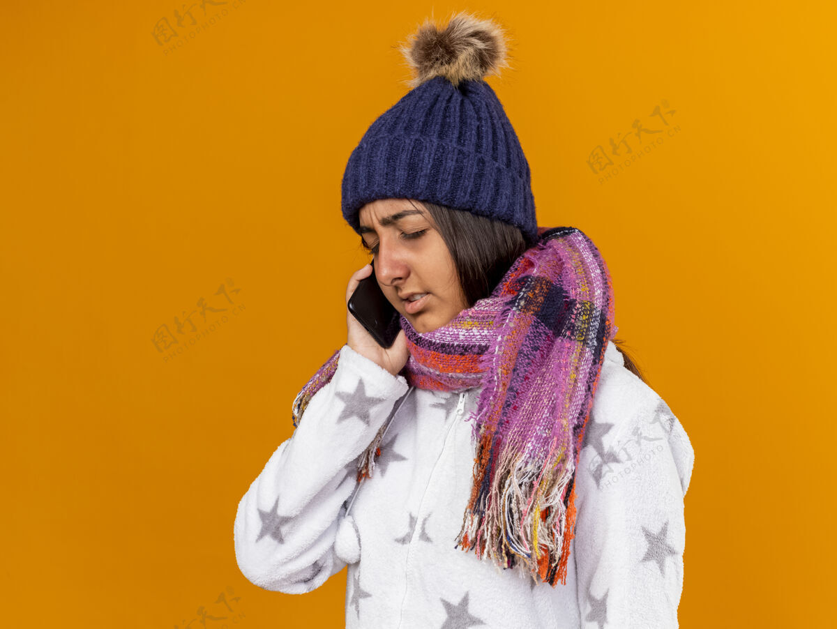 疾病未被释放的年轻病女孩闭着眼睛戴着冬季帽子围巾讲电话隔离在黄色背景帽子电话围巾