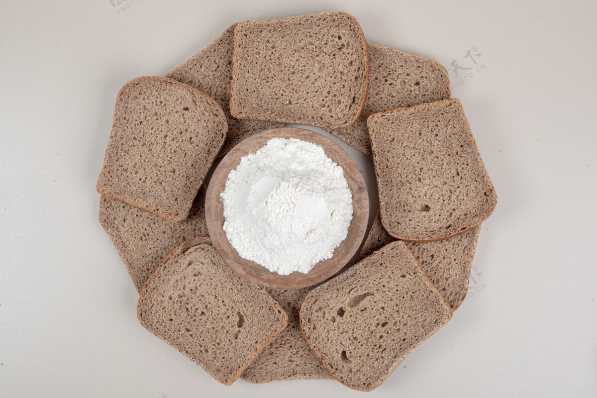 切切片新鲜的棕色面包和木制的面粉碗在白色的表面烘焙硬皮木材
