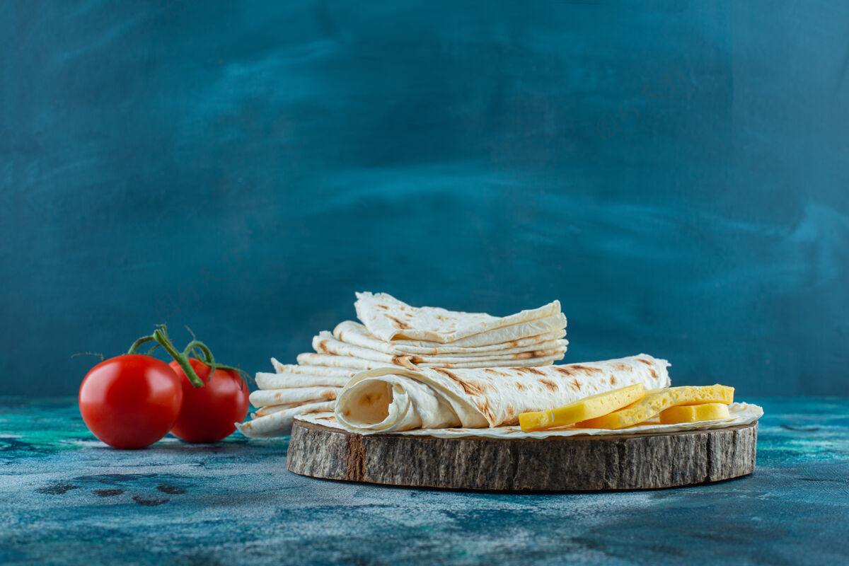 拉瓦什在蓝色背景上 番茄旁边的一块板上放上拉瓦什和奶酪糕点烘焙美食