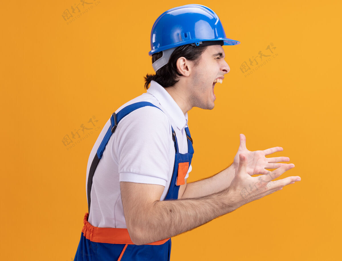 好斗身穿施工制服 头戴安全帽的年轻建筑工人站在橘色的墙上高喊着 表情咄咄逼人男人站立头盔