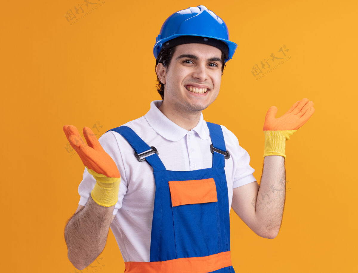 年轻身穿施工制服 头戴安全帽的年轻建筑工人站在橙色的墙上 面带微笑地看着前方快乐制服微笑