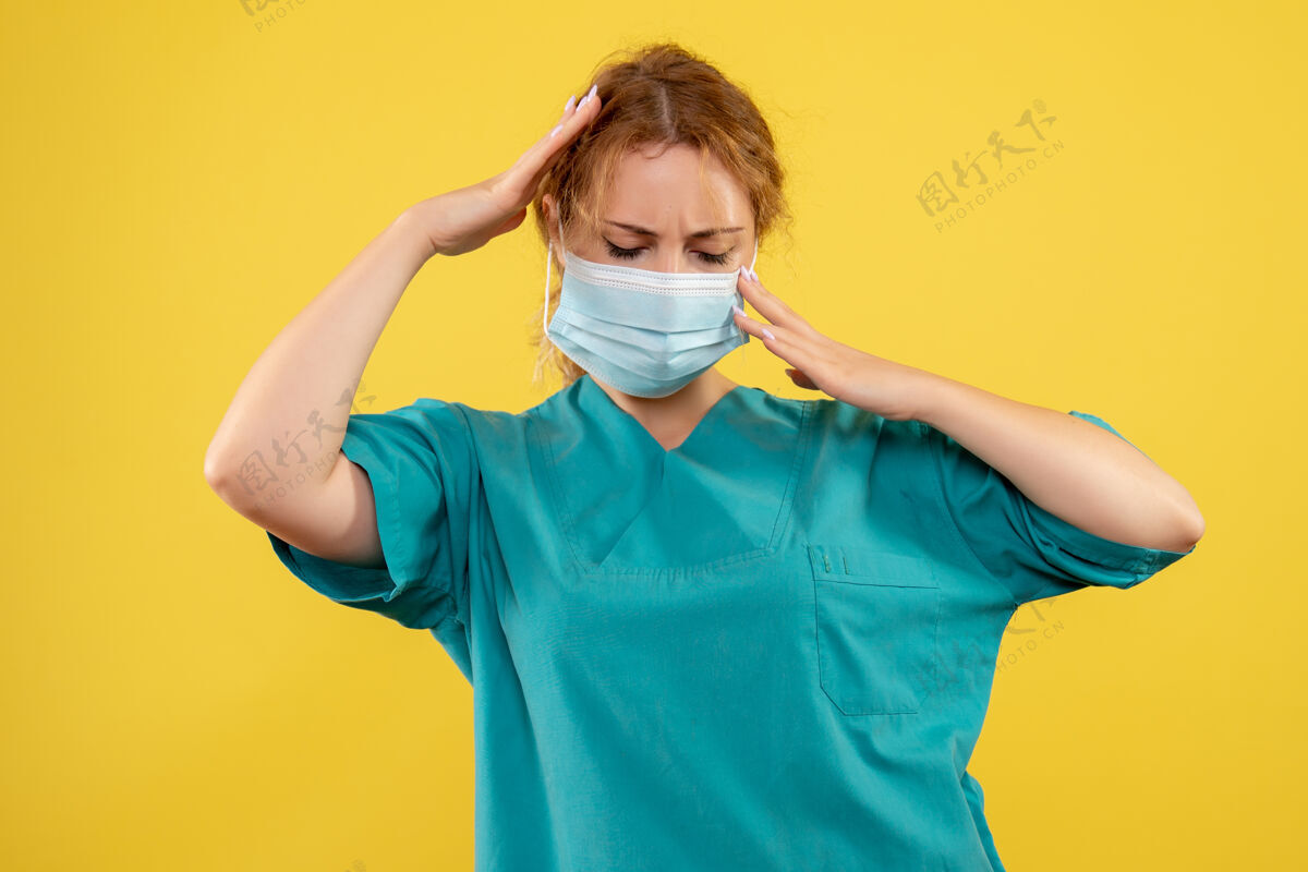 前面黄墙上年轻的女医生穿着医疗服 戴着头痛的面罩人医学面具