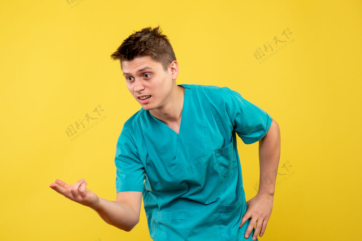 前面黄色墙壁上穿着医疗服的男医生的正视图医学肖像快乐