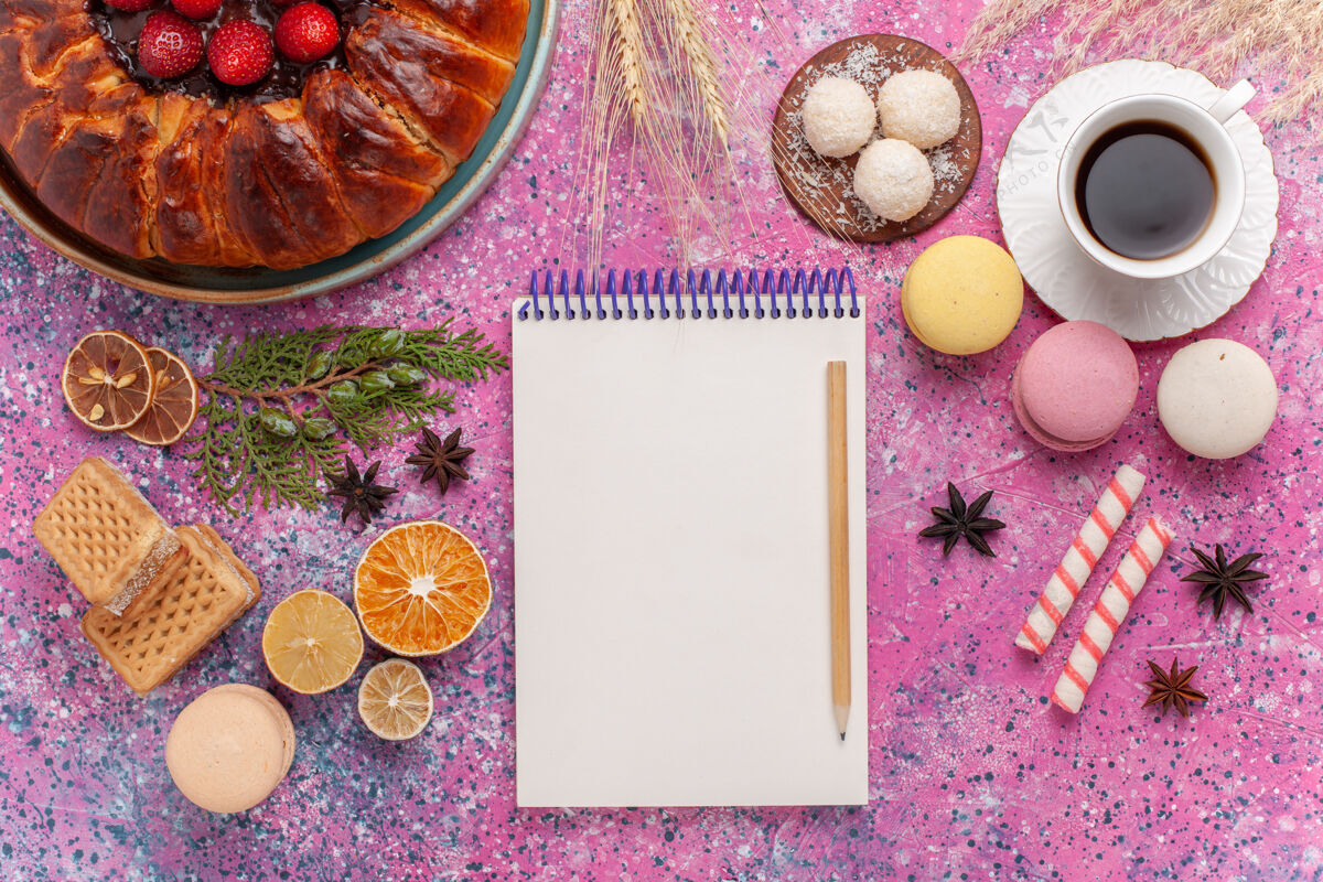 笔记本俯瞰美味的草莓派和华夫饼和法国马卡龙放在粉红色的蛋糕上糖果蛋糕草莓
