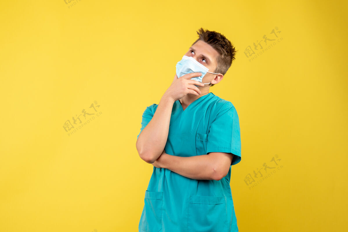 人穿着医疗服 戴着防护面罩的男医生的正面图在黄色的墙上思考医院套装正面