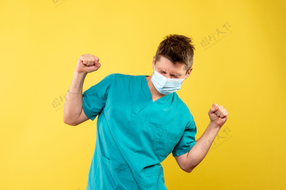 人身着医疗服 戴着无菌口罩的男医生正站在黄色的墙上欢呼雀跃健康帅哥成人