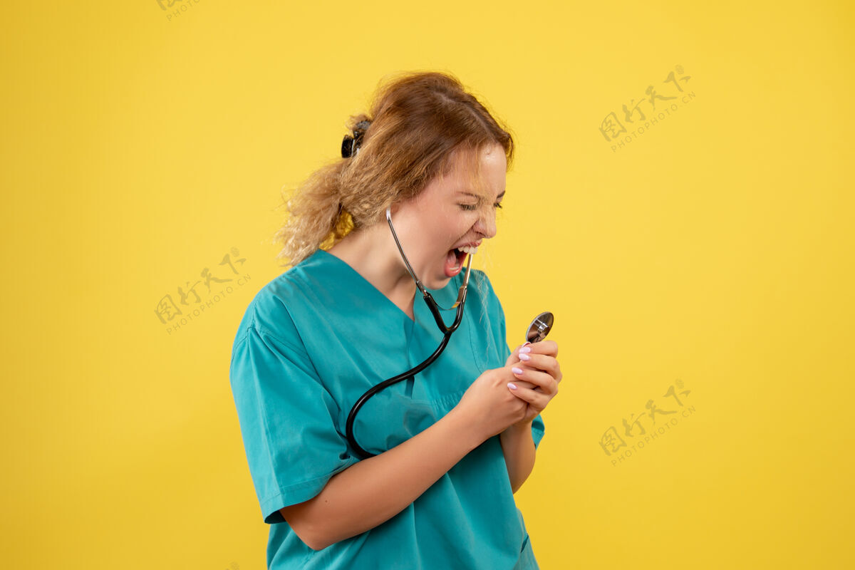 女医生黄色墙壁上穿着医疗服的女医生对着听诊器尖叫的正视图健康医疗器械病毒
