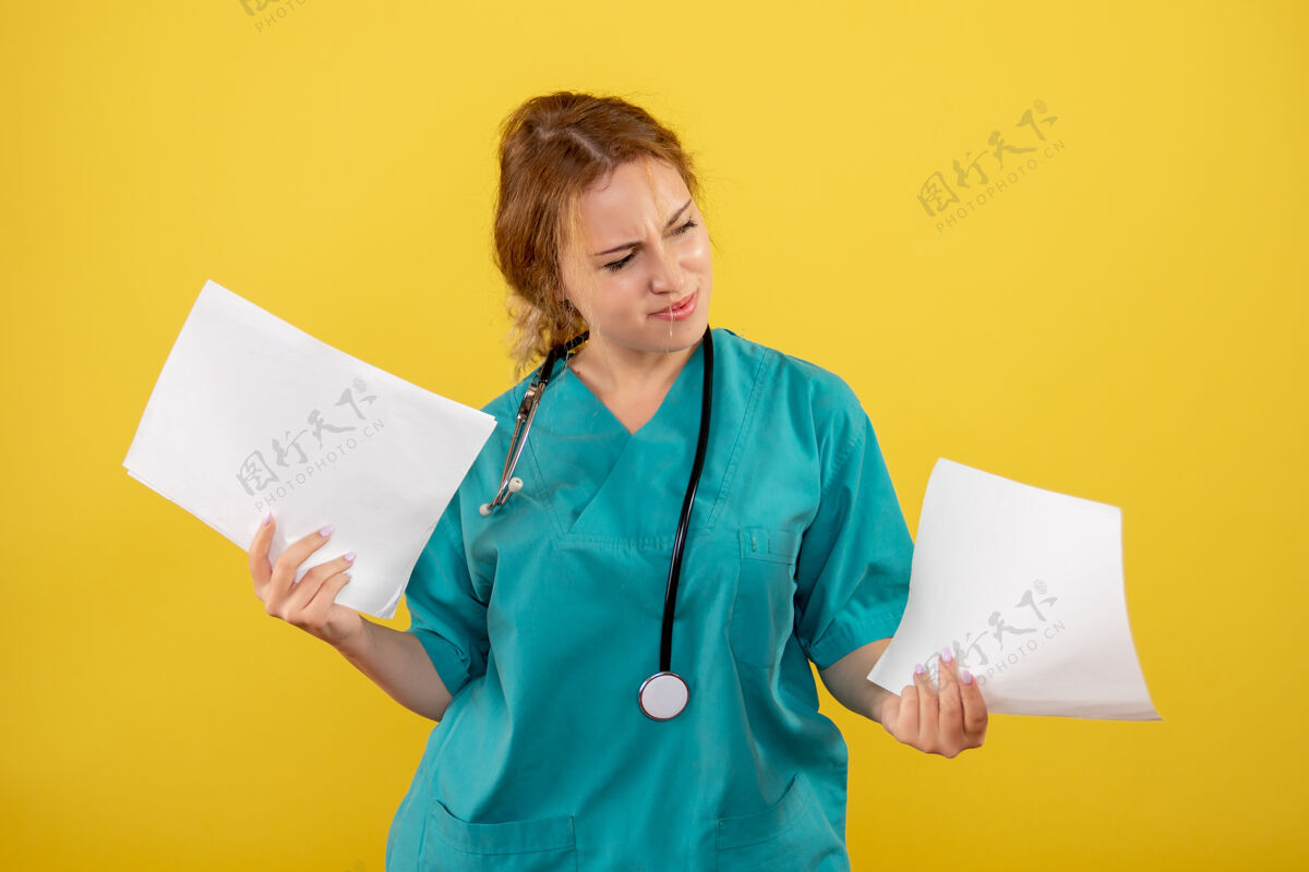 人黄色墙壁上穿着医疗服的女医生手持分析的正面图女医生医院听诊器