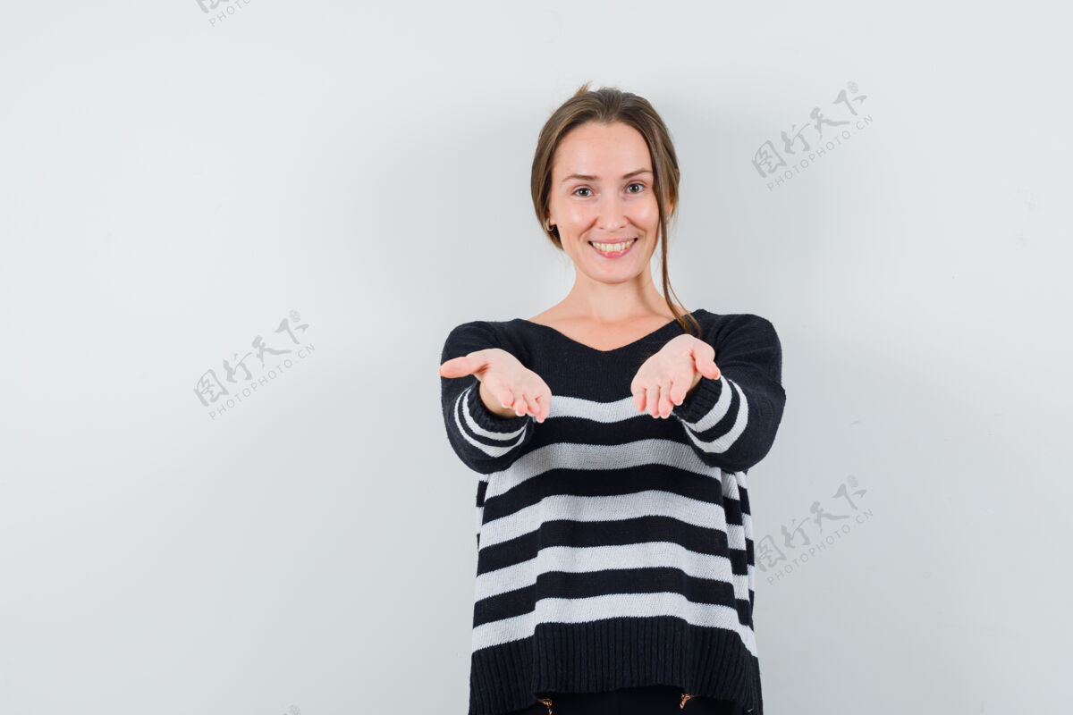 人一位年轻的女士 穿着条纹针织衫和黑色裤子 伸出手 看起来很开心时尚干净东西