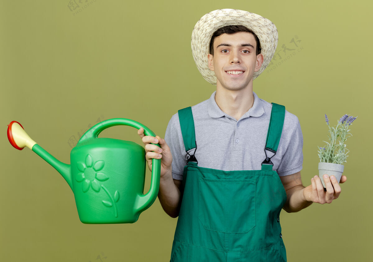 穿着微笑的年轻男园丁戴着园艺帽 在花盆和浇水罐里捧着花花浇水复制