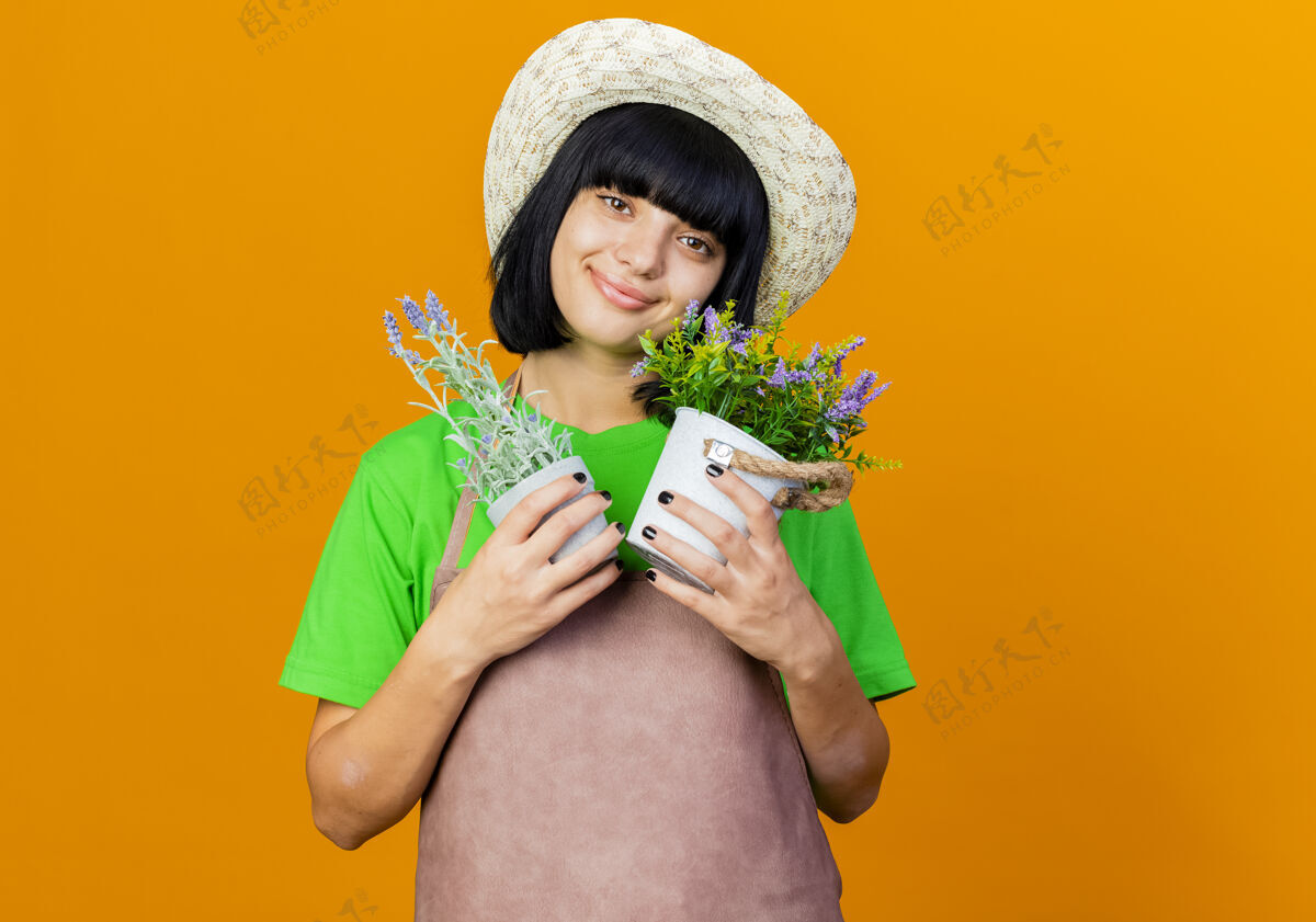 女高兴的年轻女园丁穿着制服戴着园艺帽拿着花盆年轻复制园艺
