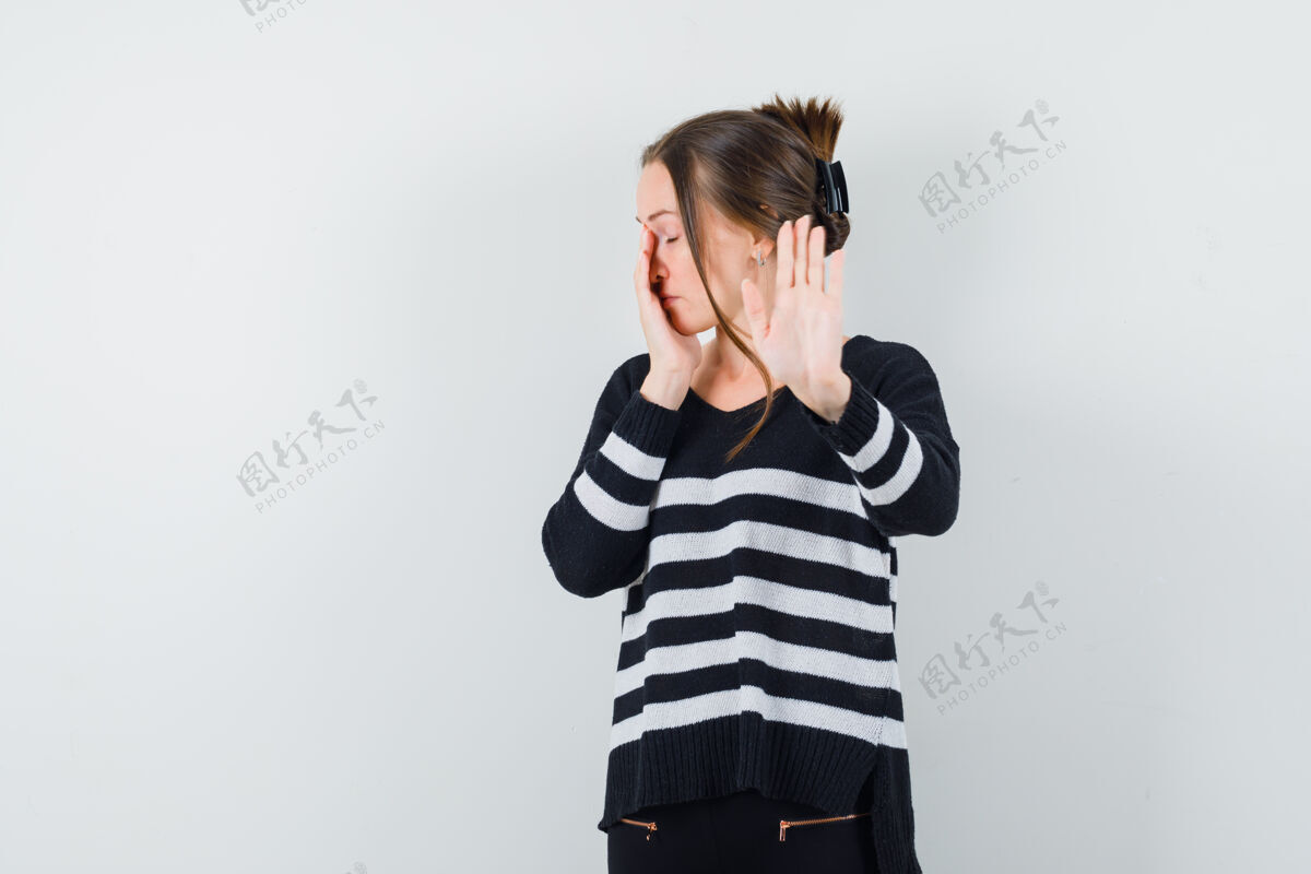 健康穿着条纹针织衫和黑色裤子的年轻女子 展示停车标志 用手捂住脸的一部分 看上去很忧郁黑发健康快乐