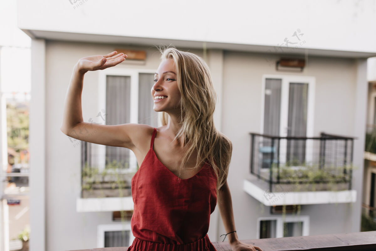 女性穿着睡衣的幸福晒黑的女人微笑着挥舞着手站在阳台上的高加索女模特令人惊叹阳台光女人