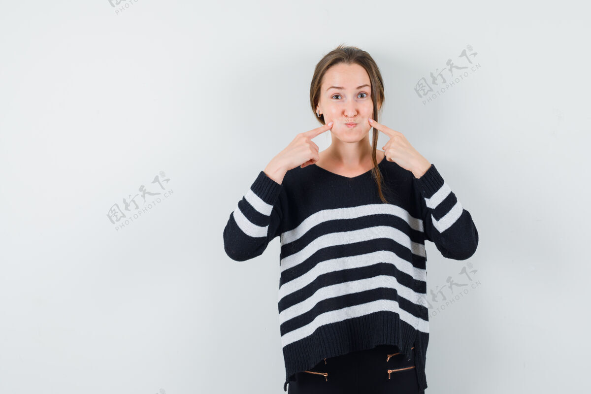 吹一位穿着休闲衬衫的年轻女士用手指抚摸着脸颊 看上去很滑稽肖像微笑时尚