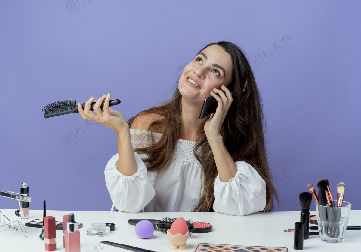 女人笑容可掬的美女拿着化妆工具坐在桌边拿着梳子讲着电话孤零零地看着紫色的墙上紫色发夹头发
