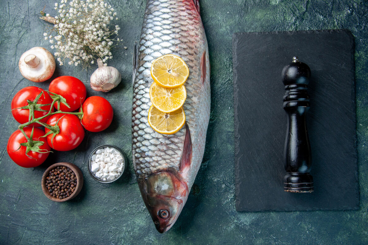 晚餐顶视图新鲜的生鱼肉与柠檬和西红柿在深蓝色的背景深色柠檬晚餐