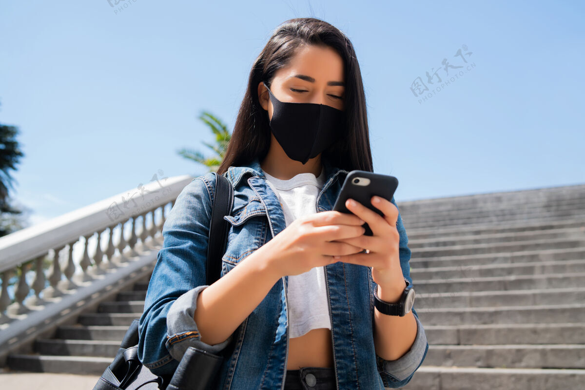 电话一张年轻女子戴着防护面具 站在街上用手机的照片城市手机手持