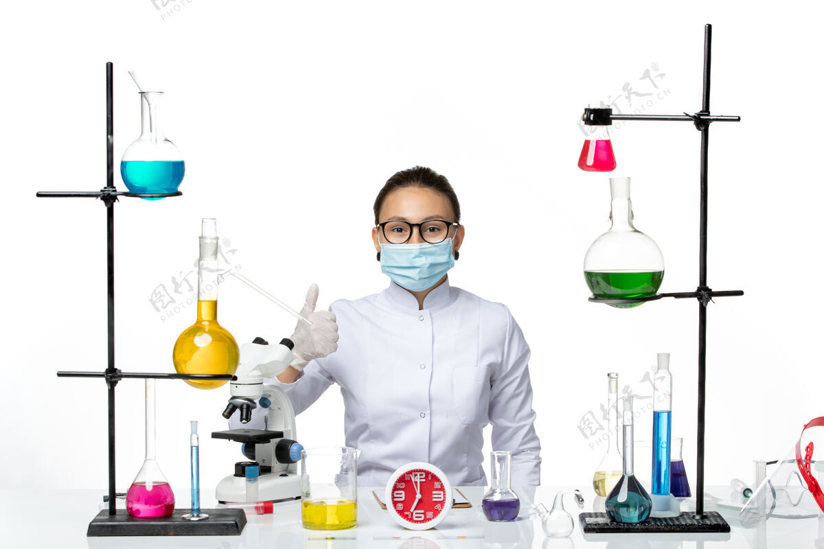 烧杯前视图穿着白色医疗服的女化学家带着面罩坐在白色背景上的溶液化学家病毒科维德飞溅实验室面具喷溅医学
