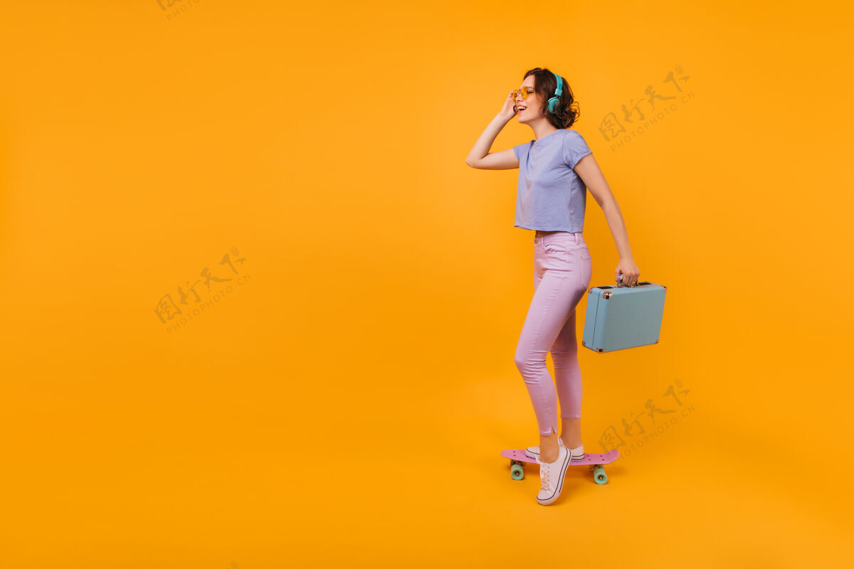 女性一位穿着白色胶鞋 身材匀称的女士正拿着蓝色的手提箱摆姿势一位幽默的短发女士站在长板上的照片人肖像多彩