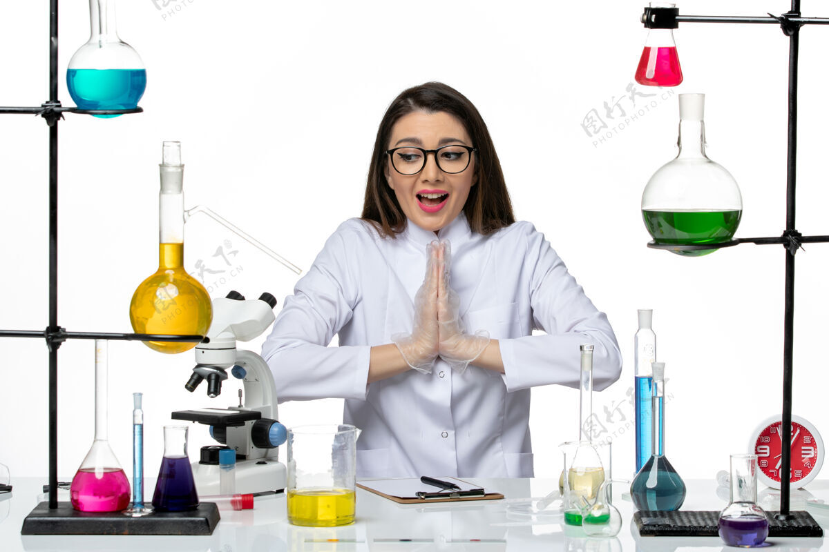 药剂师前视图：穿着白色医疗服的女化学家坐在白色办公桌上 摆姿势 实验室科学病毒柯维德大流行实验室专业科学