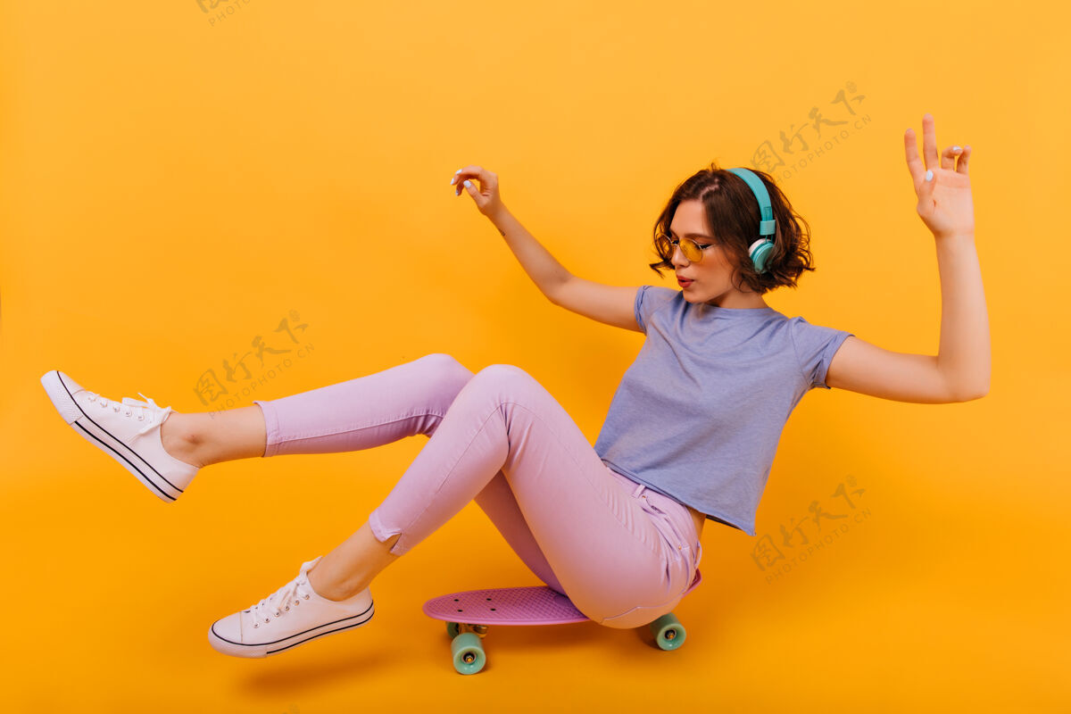 快乐坐在长板上纹身的时髦女孩留着短卷发的可爱女模特在滑板上摆姿势 听音乐长板休闲爱好