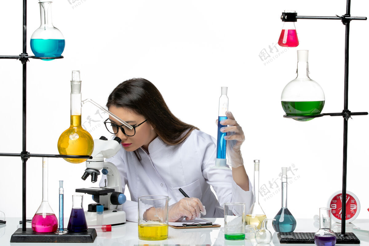 烧杯前视图穿着白色医疗服的女化学家拿着装有溶液的烧瓶 在白色背景上使用显微镜科学病毒冠状病毒-大流行实验室医学视图大流行
