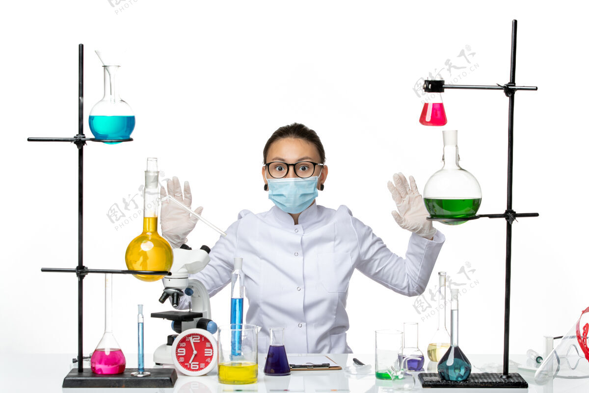 实验室前视图穿着医疗服的女化学家 带着面罩坐在桌子前面 白色背景上有溶液病毒化学实验室的covidsplash药医疗前面