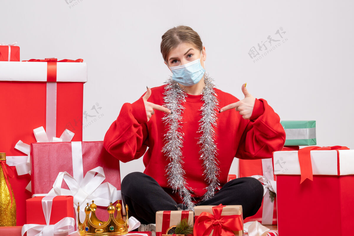 成人正面图：年轻女性戴着无菌面具坐着 手里拿着圣诞礼物坐着礼物病毒