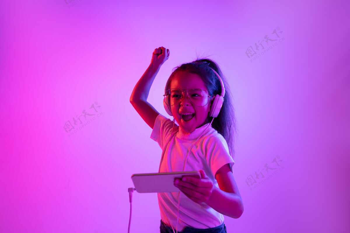 童年美丽的女性肖像被隔离在霓虹灯下的紫色背景上戴着眼镜的情感女孩人类的情感 面部表情概念跳舞 听音乐 游戏和胜利面部惊讶小